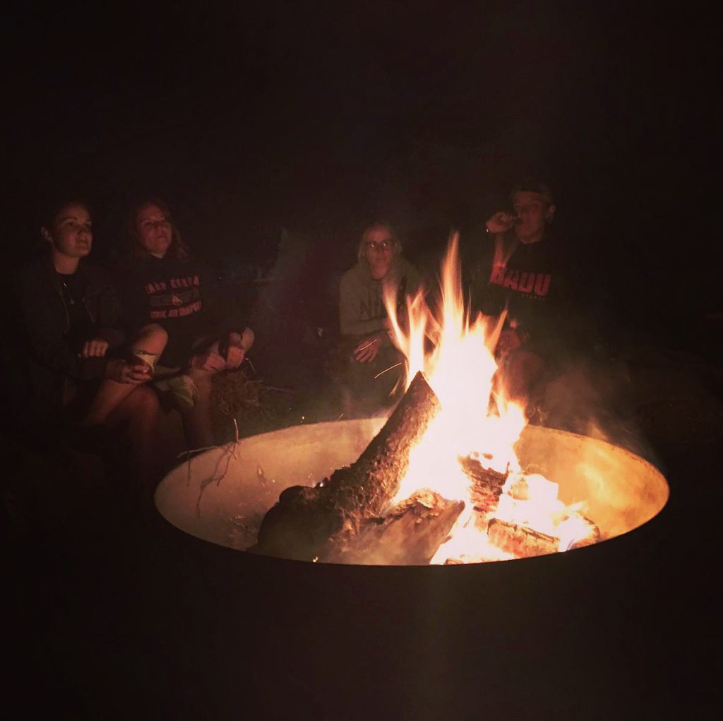 A photo of a group of friends enjoying a beverage around a roaring fire bowl in the darkness at Ranby Hill Fest